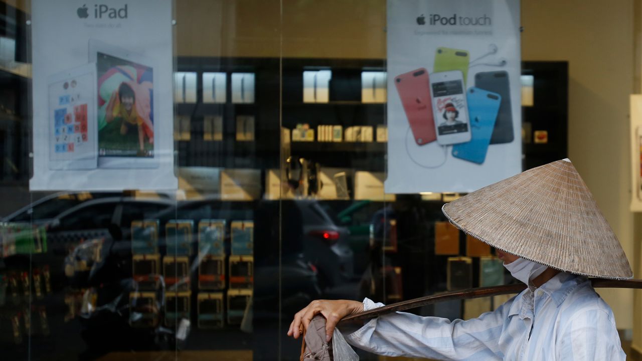 A fruit vendor walking past an Apple store in Hanoi 